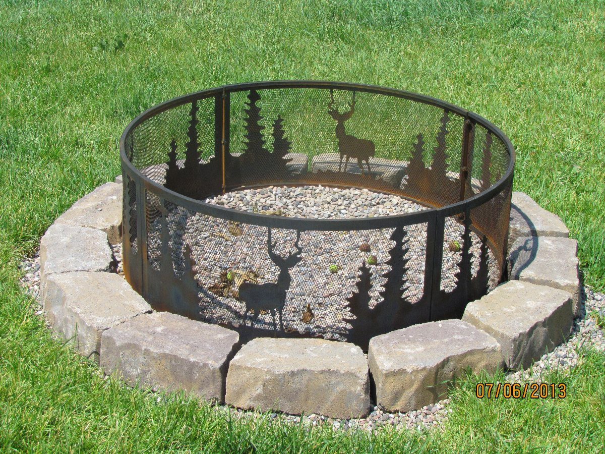 A decorative metal fire ring with deer silhouettes sits within a stone-bordered gravel fire pit.