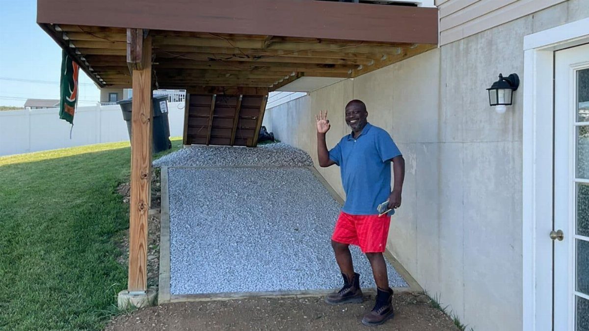 A man smiling next to a gravel-covered area underneath a wooden deck structure.